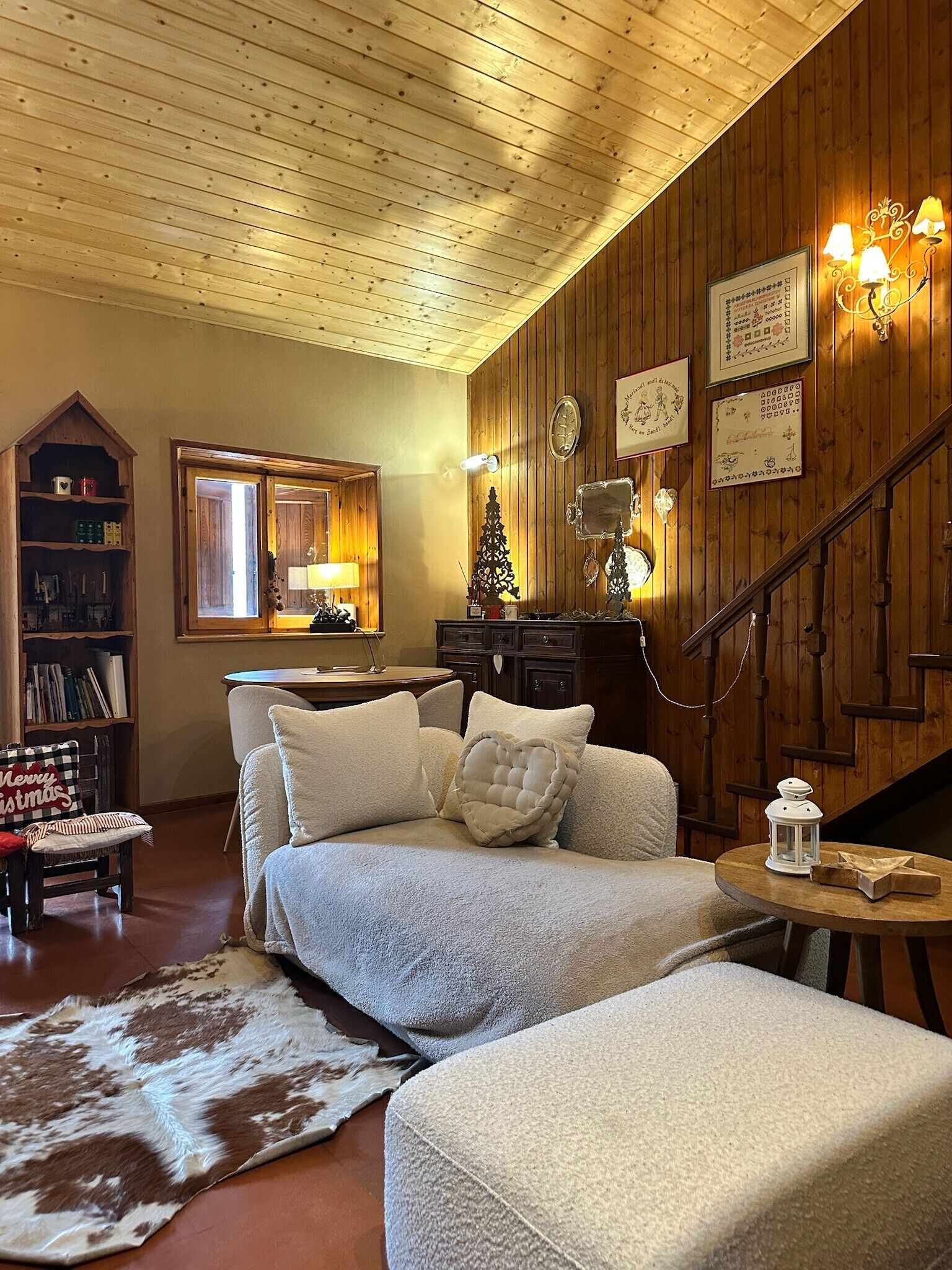 A cozy living room with a wooden ceiling, a fireplace, a sofa set, a bookshelf, and a staircase.