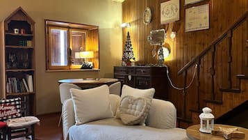 A cozy living room with a wooden ceiling, a fireplace, a sofa set, a bookshelf, and a staircase.