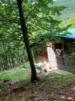 A rustic stone building with a green roof, surrounded by a forested area.