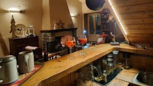 Une pièce chaleureuse avec une cheminée, un plafond en bois et un coin bar équipé de verres et de tasses.