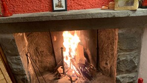 Une cheminée avec un feu, un tableau encadré posé sur le manteau de la cheminée et un fauteuil rouge.