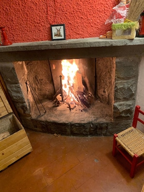 A fireplace with a fire, a framed picture on the mantel, and a red chair.