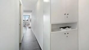 Ein moderner Flur mit weißen Wänden, einer Glastür am Ende und einem weißen Schrank mit Schubladen und Regalen.
