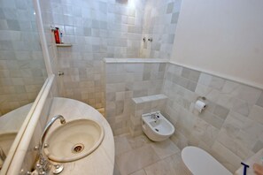 Une salle de bain équipée d’un lavabo, d’un bidet, de toilettes et de murs carrelés.