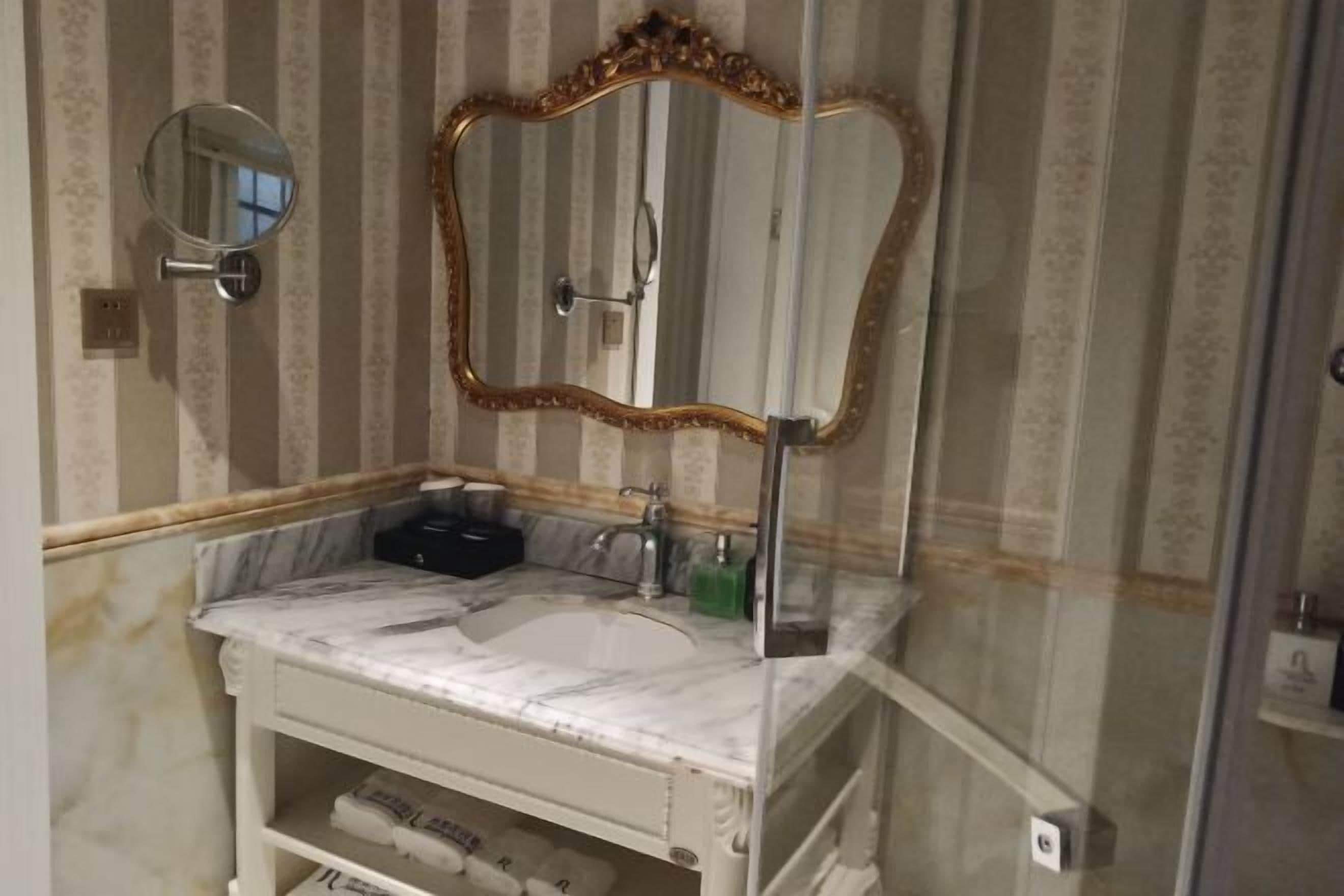 A bathroom with a marble sink, a round mirror, and a gold-framed mirror.