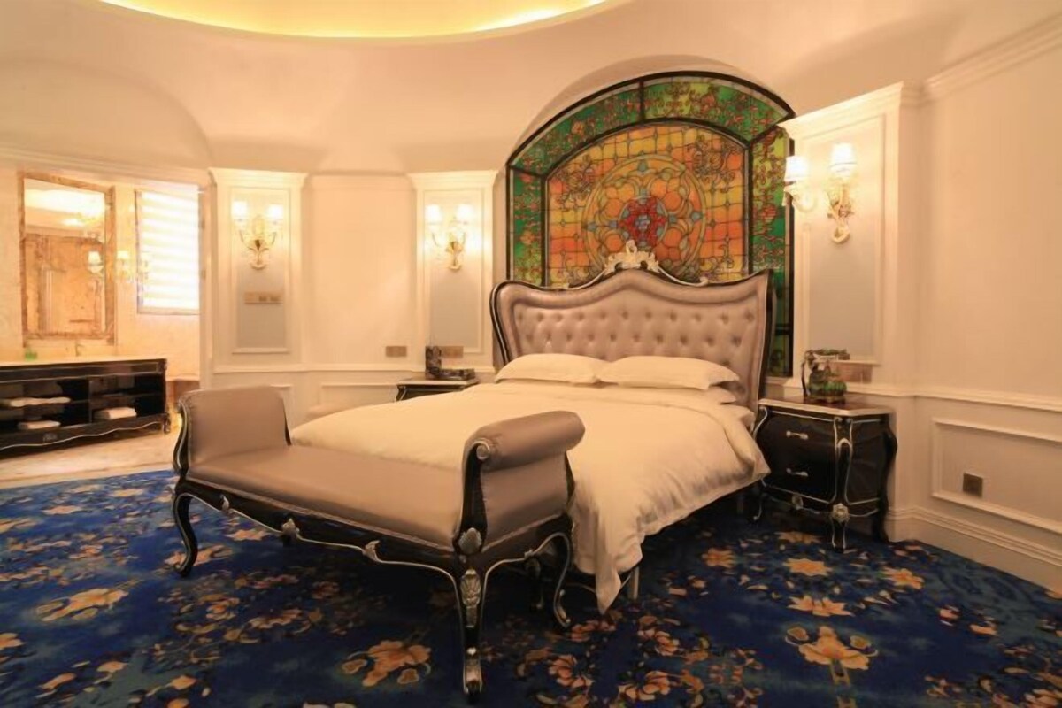 Une chambre spacieuse avec un grand lit, un banc et une fenêtre à vitraux au-dessus du lit.