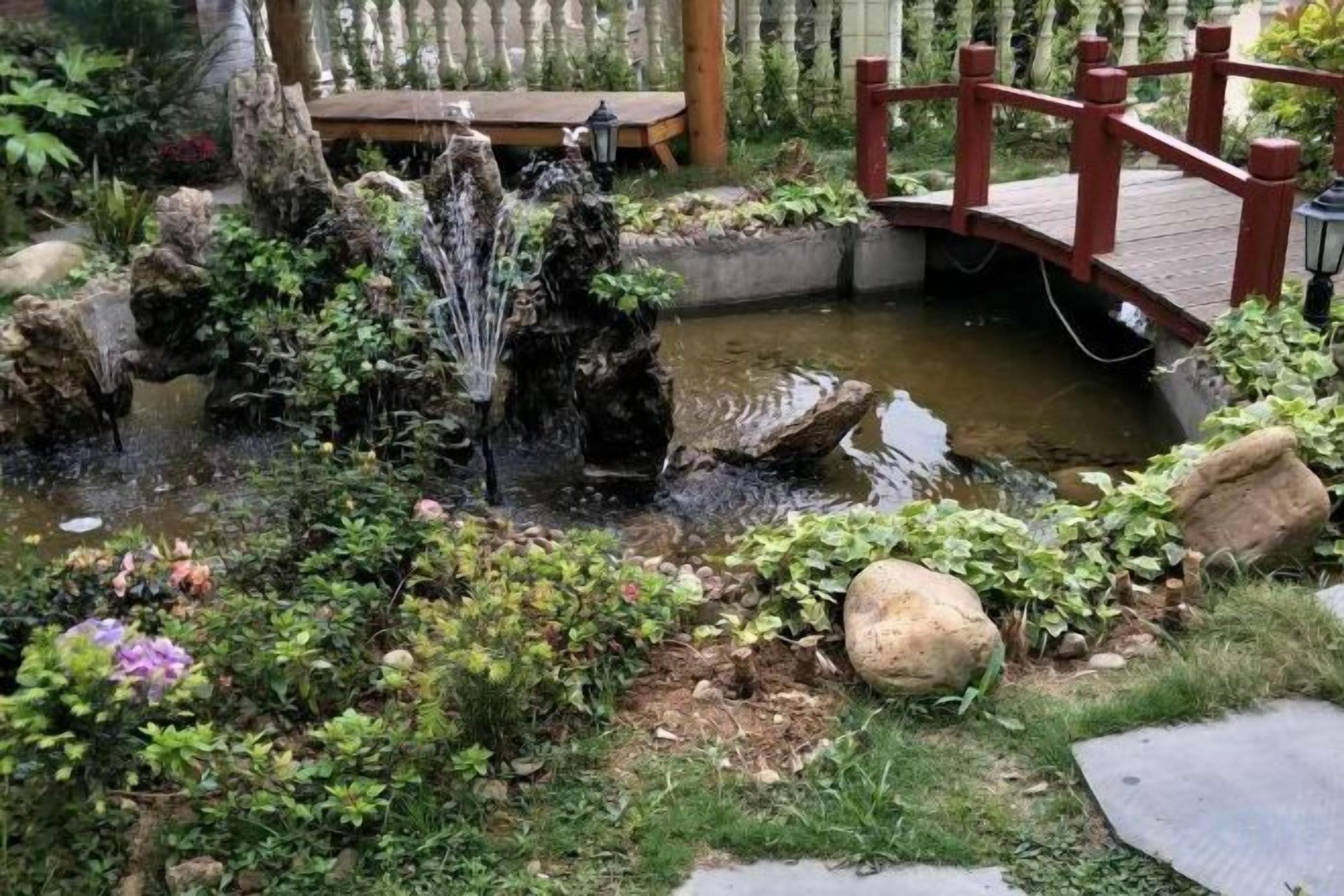 A garden with a pond, a wooden bridge, and a wooden deck.