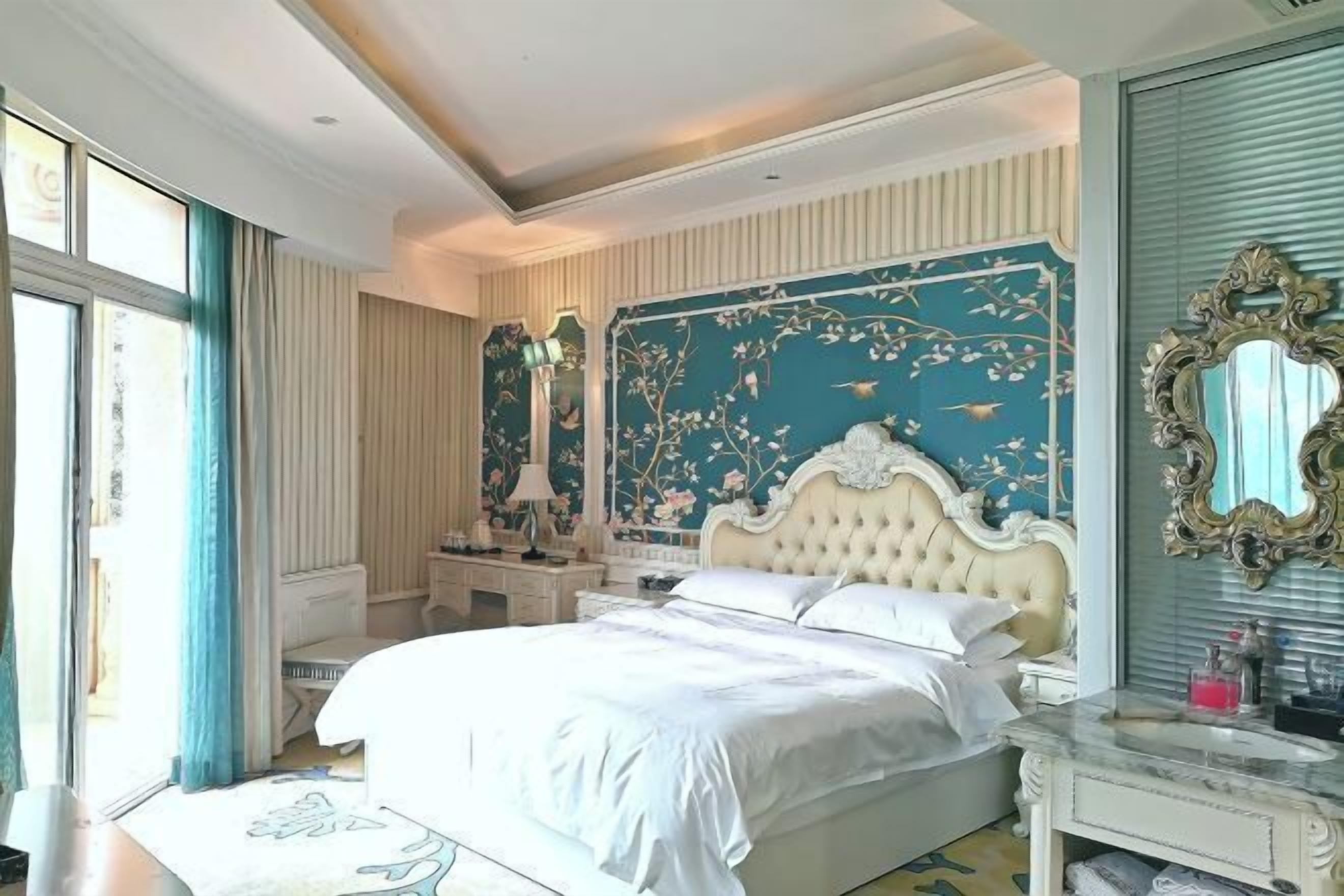 A bedroom with a large bed, a vanity with a mirror, and a floral wallpaper design.