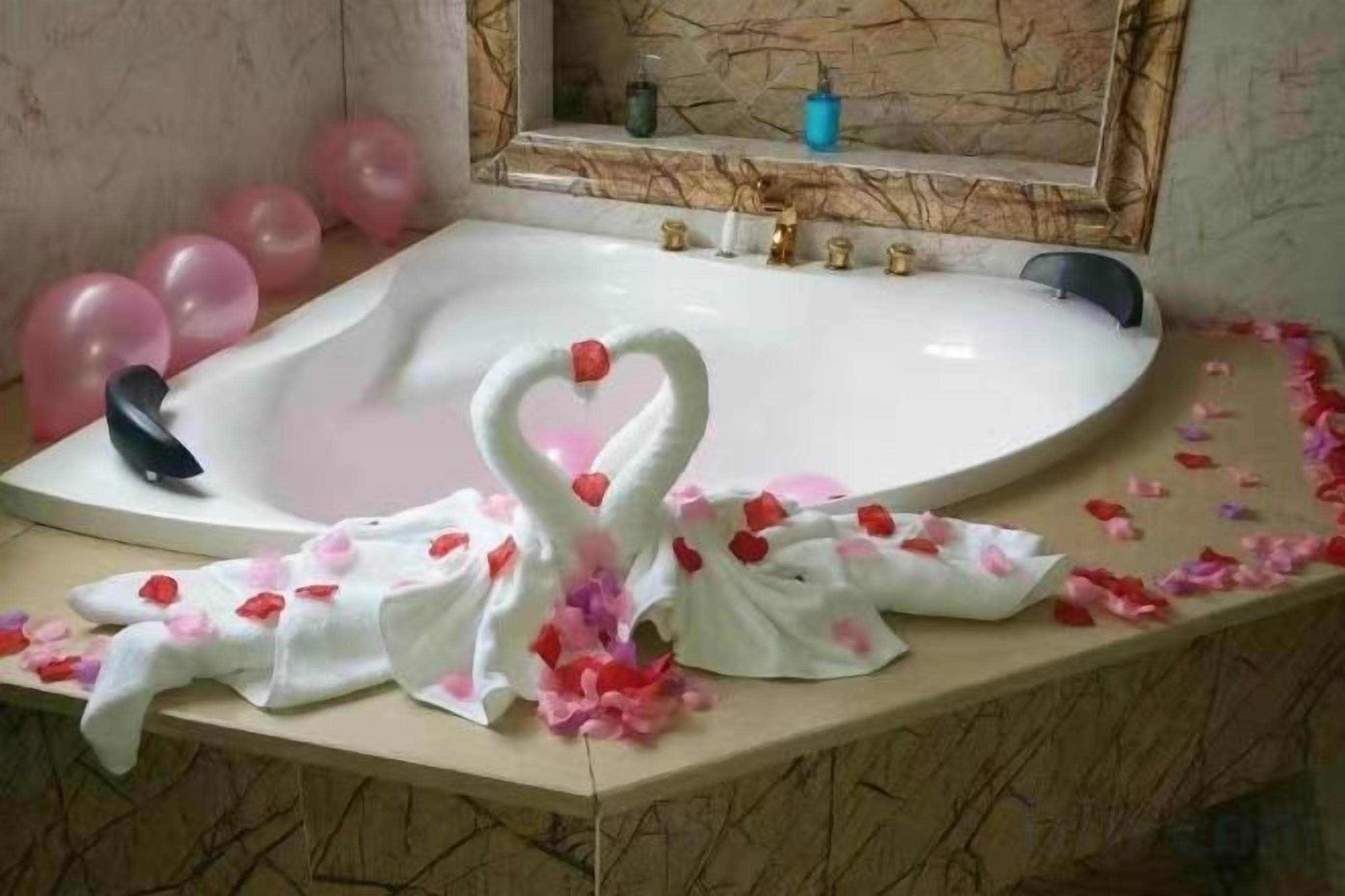 A bathroom with a bathtub, a mirror, and pink balloons.