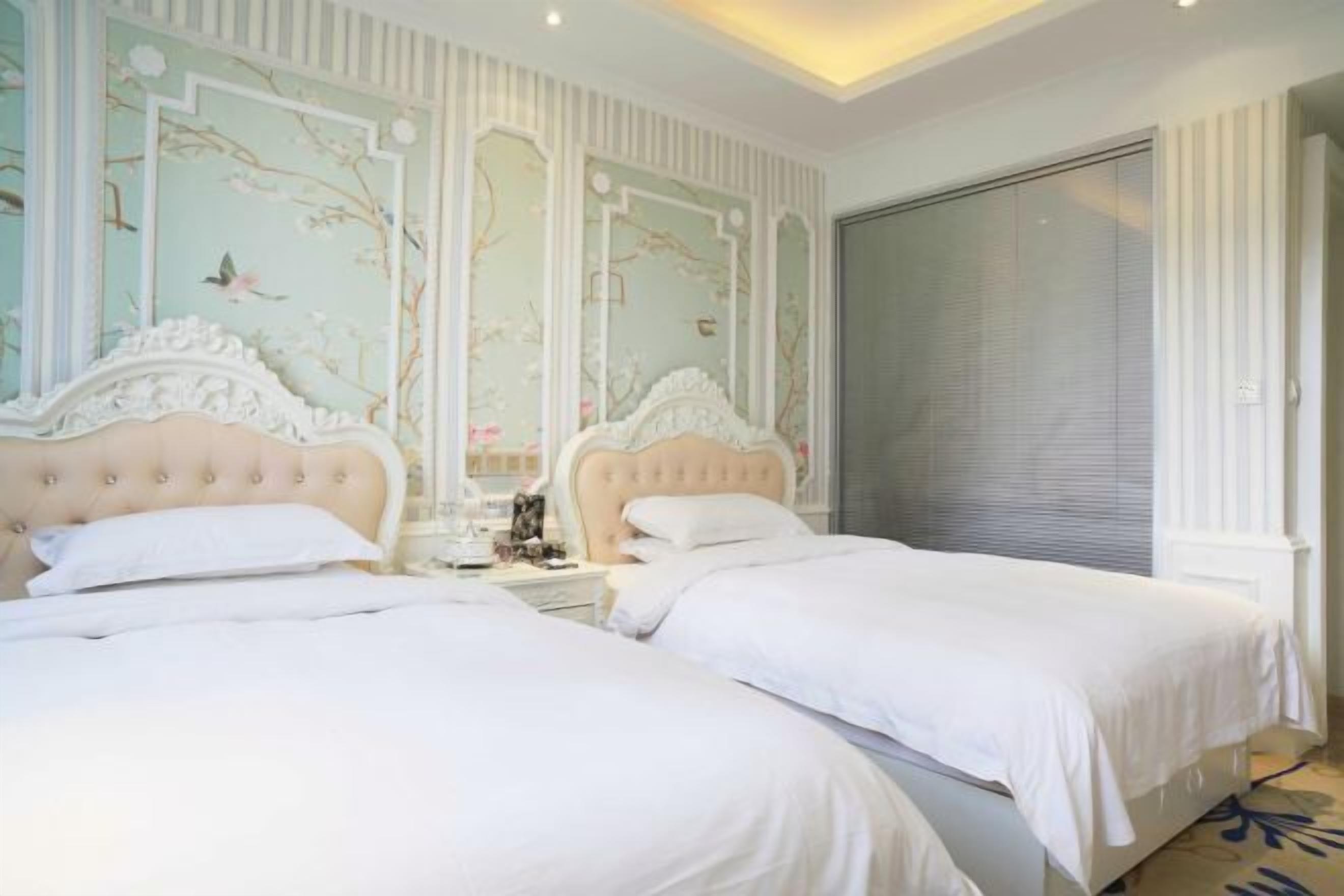 A bedroom with two beds, a large window, and a decorative wall.