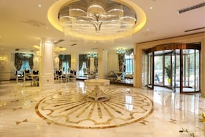 Un hall d’entrée luxueux avec un sol circulaire en marbre, de magnifiques lustres et une entrée en verre.