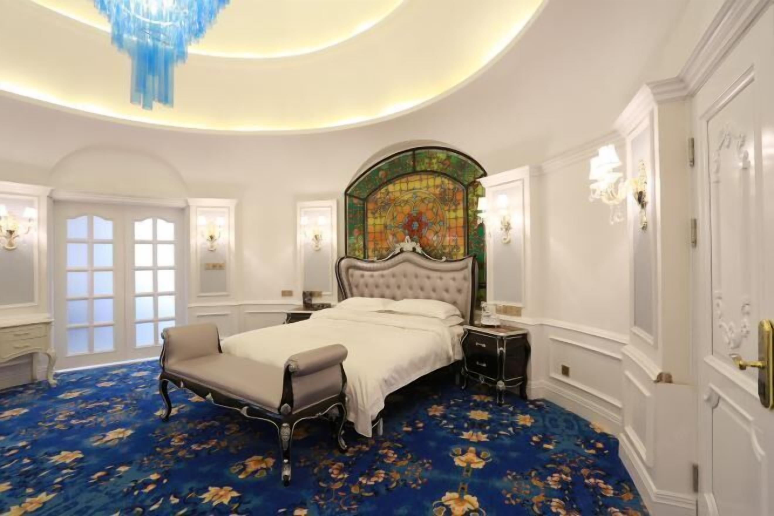 A luxurious bedroom with a large bed, a chandelier, and a floral carpet.