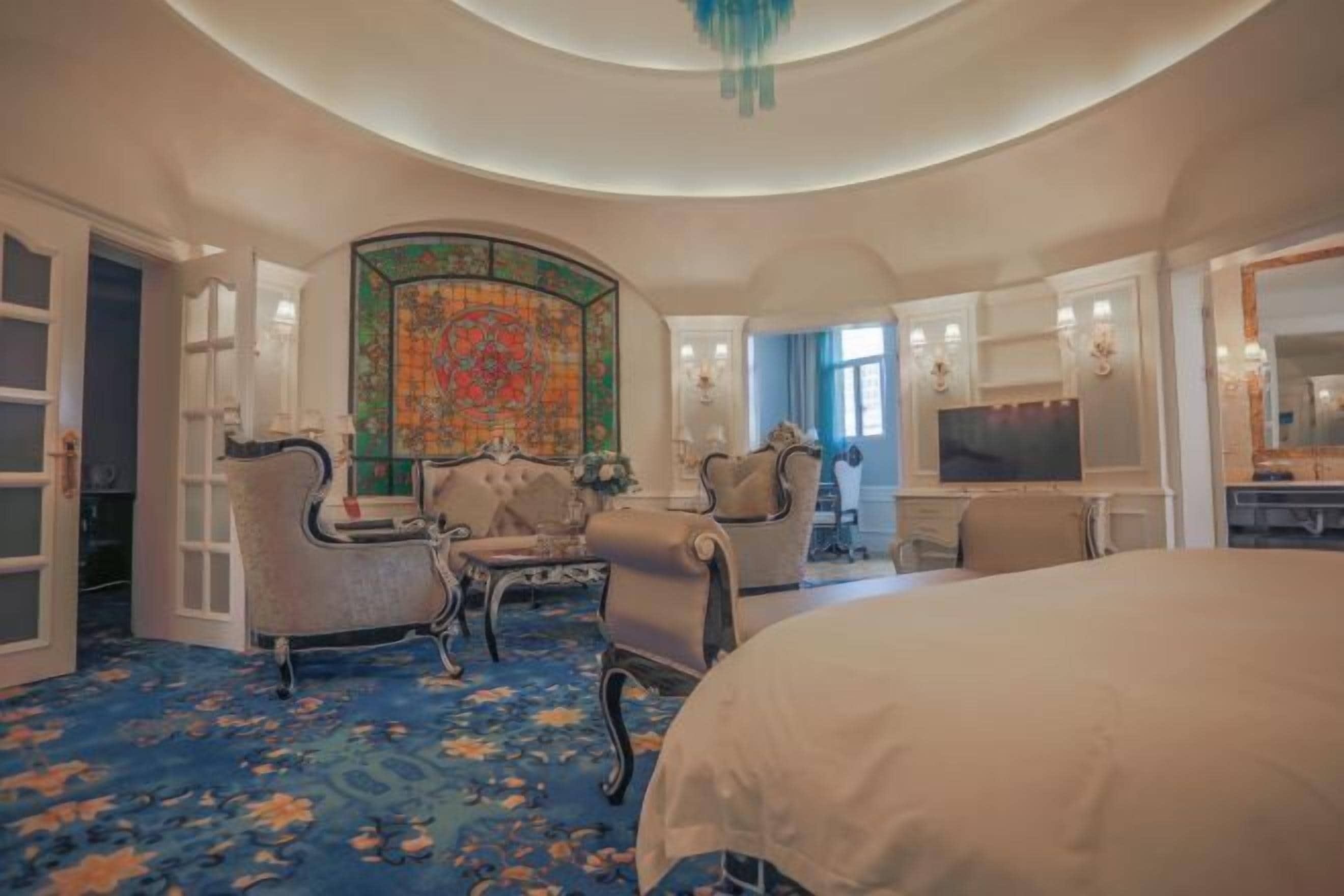 A hotel room with a large bed, two armchairs, a small table, a TV, and a decorative wall.