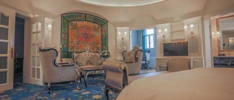 A hotel room with a large bed, two armchairs, a small table, a TV, and a decorative wall.