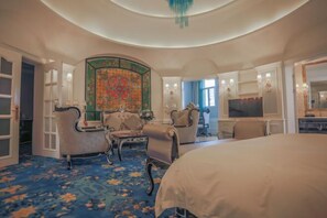 Une chambre d’hôtel avec un grand lit, deux fauteuils, une petite table, un téléviseur et un mur décoratif.