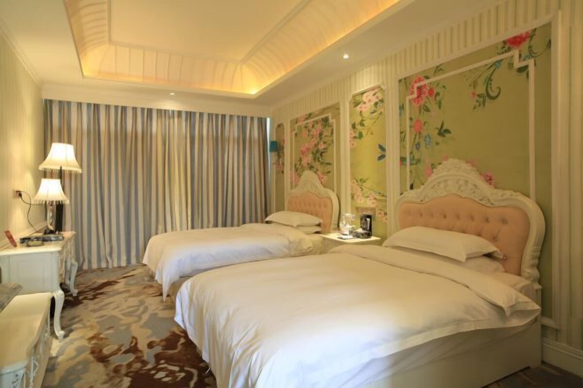 Une chambre d’hôtel avec deux lits, un bureau, une lampe et un papier peint à motifs floraux.