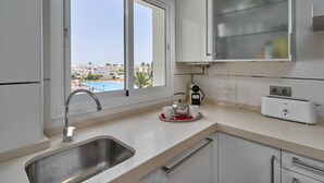 Une cuisine moderne dotée d’un évier en acier inoxydable, d’une fenêtre offrant une vue sur les immeubles, d’un grille-pain et d’un meuble avec une porte en verre.