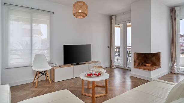 Un salon moderne doté d’un téléviseur à écran plat, d’un canapé blanc, d’une table à manger avec un plateau et d’une cheminée.