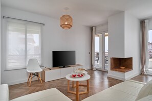 En moderne stue med et fladskærms-tv, en hvid sofa, et spisebord med et fad og en pejs.