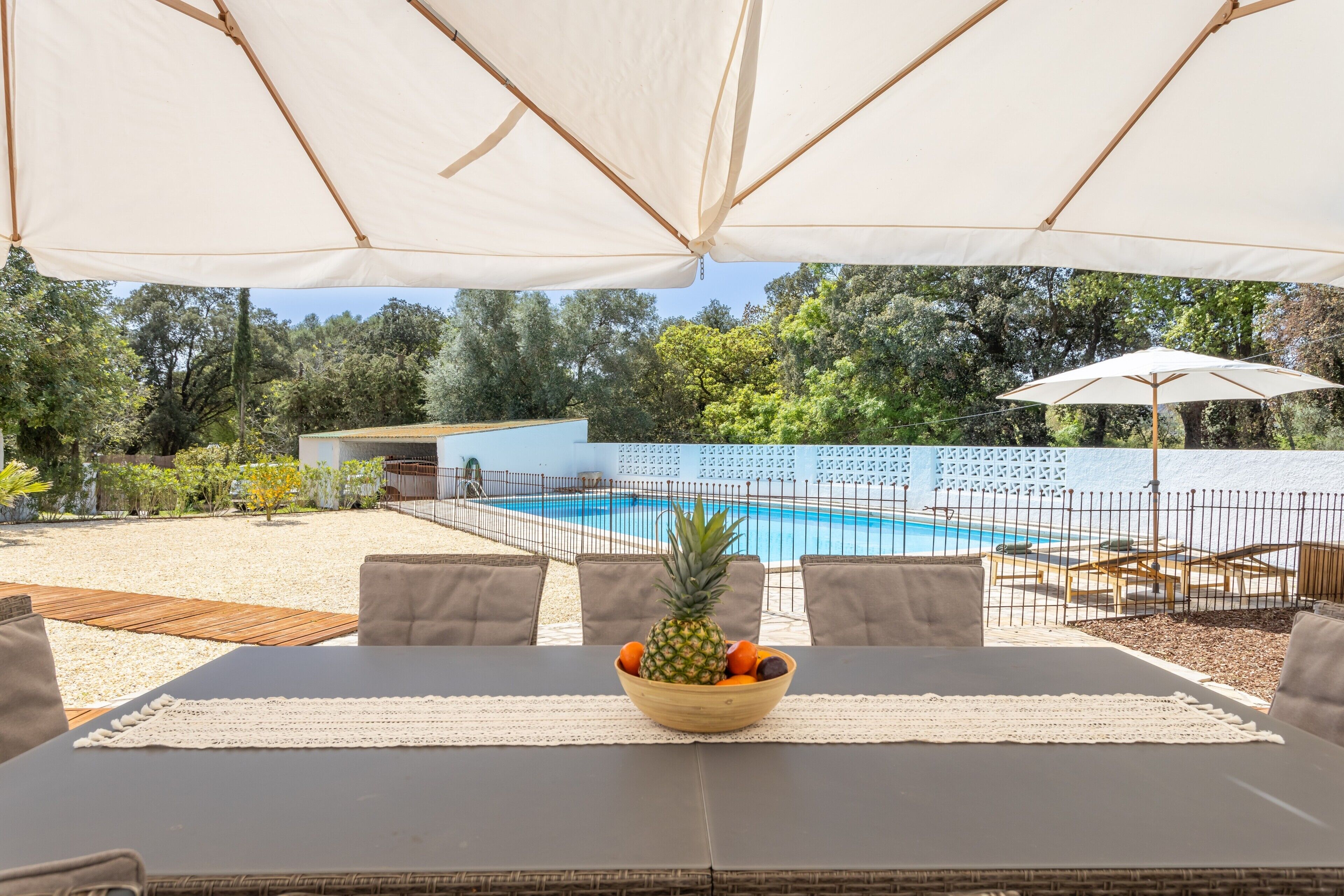 An outdoor dining area with a pool view, covered by large umbrellas, and a table with a fruit bowl.