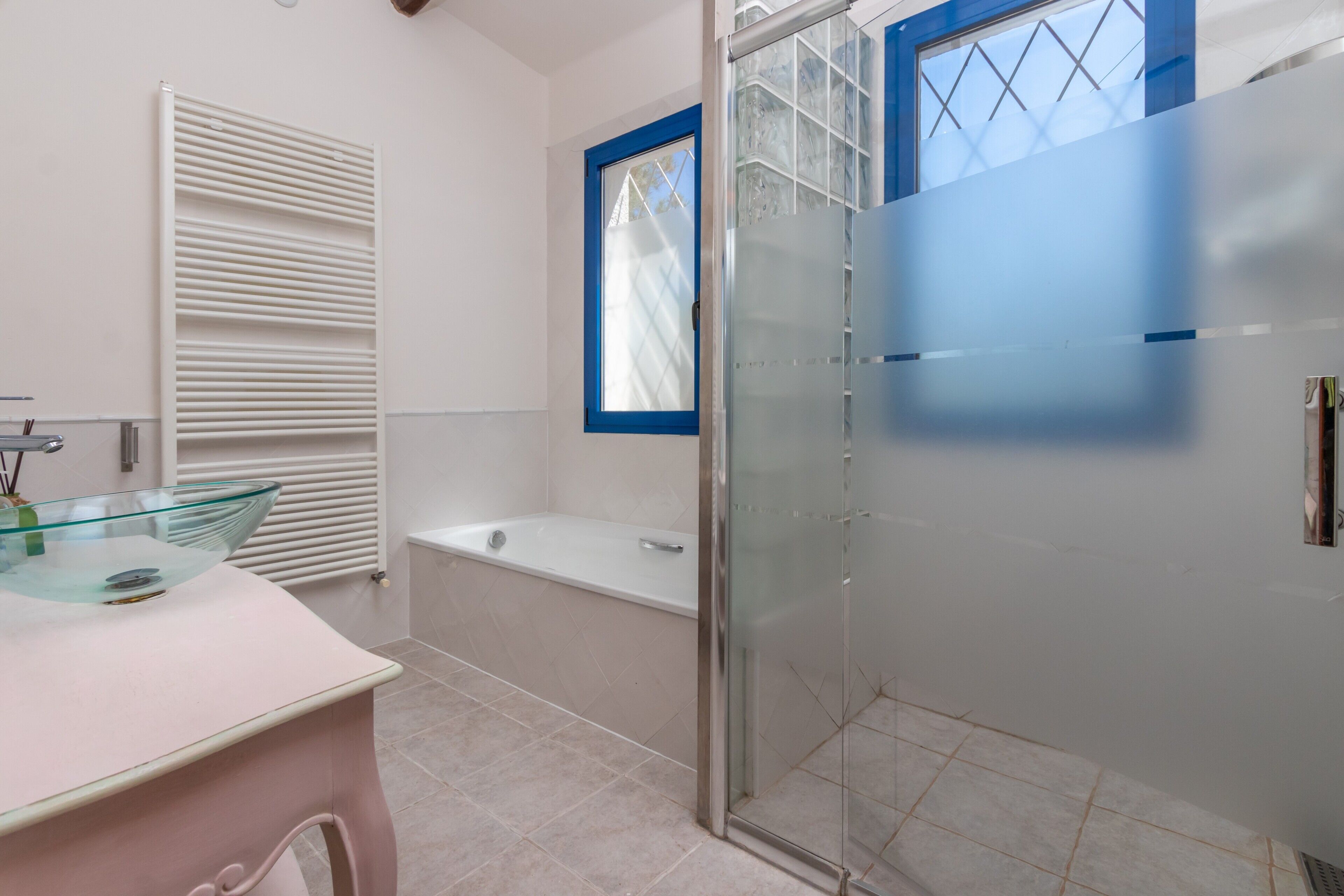 Een badkamer met een douchecabine van glas, een badkuip en een wastafel met een glazen blad.