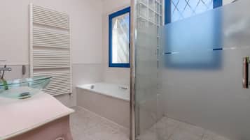 Een badkamer met een douchecabine van glas, een badkuip en een wastafel met een glazen blad.