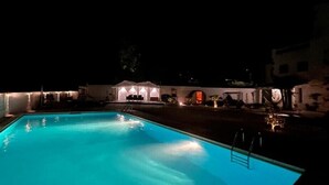 Ein Schwimmbad bei Nacht mit einem überdachten Sitzbereich und einem Gebäude im Hintergrund.