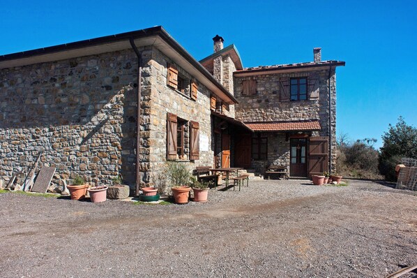 A stone building with a gravel driveway, wooden shutters, and potted plants.
