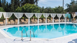 Uma piscina com água azul cristalina, rodeada por espreguiçadeiras e cortinas brancas.