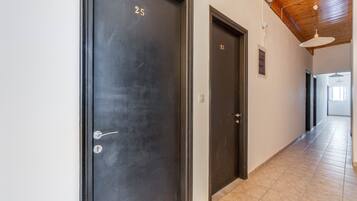 A hallway with two dark doors, numbered 25 and 23, leading to rooms. The hallway has a tiled floor and a wooden ceiling with exposed beams.
