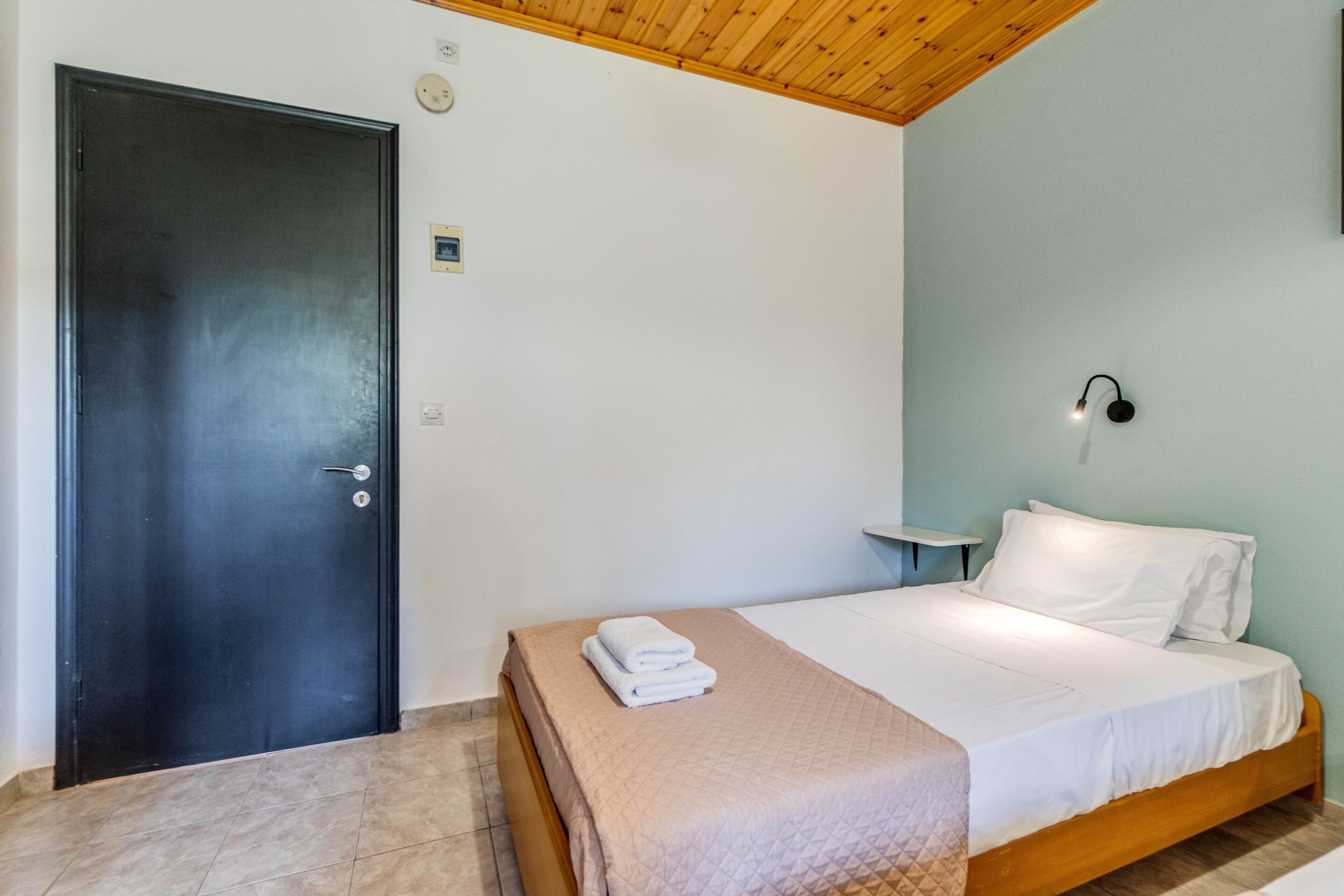 Un dormitorio con una cama, una mesita de noche, un reloj de pared y una puerta.