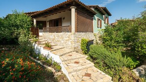 A two-story house with a stone facade, a tiled roof, and a balcony with a wooden railing.
