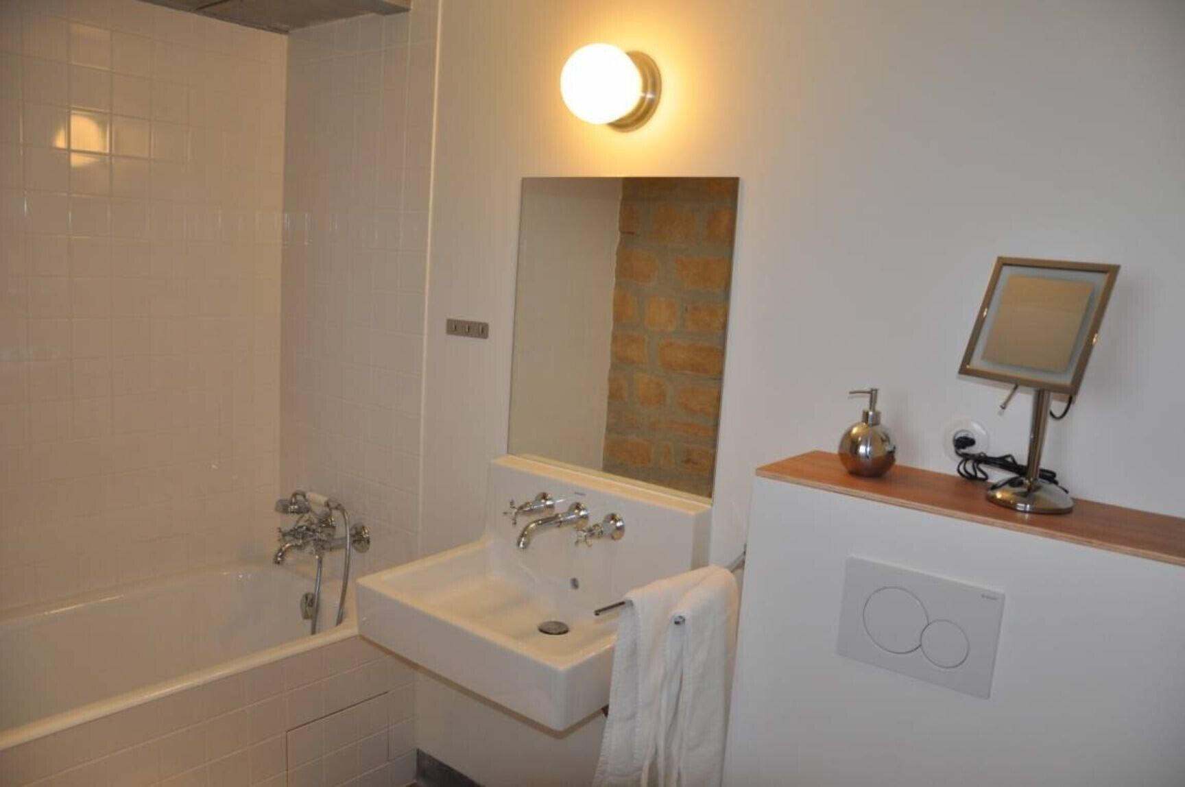A bathroom with a bathtub, a sink, a mirror, and a light fixture.