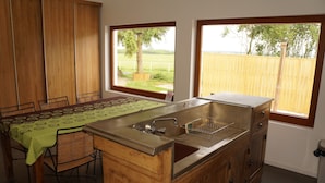 Una cocina con una isla grande, gabinetes de madera, una mesa de comedor con sillas y dos ventanas con vistas a un patio cercado.