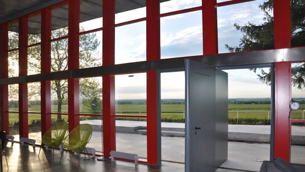 Un interior moderno con ventanas amplias, una puerta y vista a un paisaje verde.