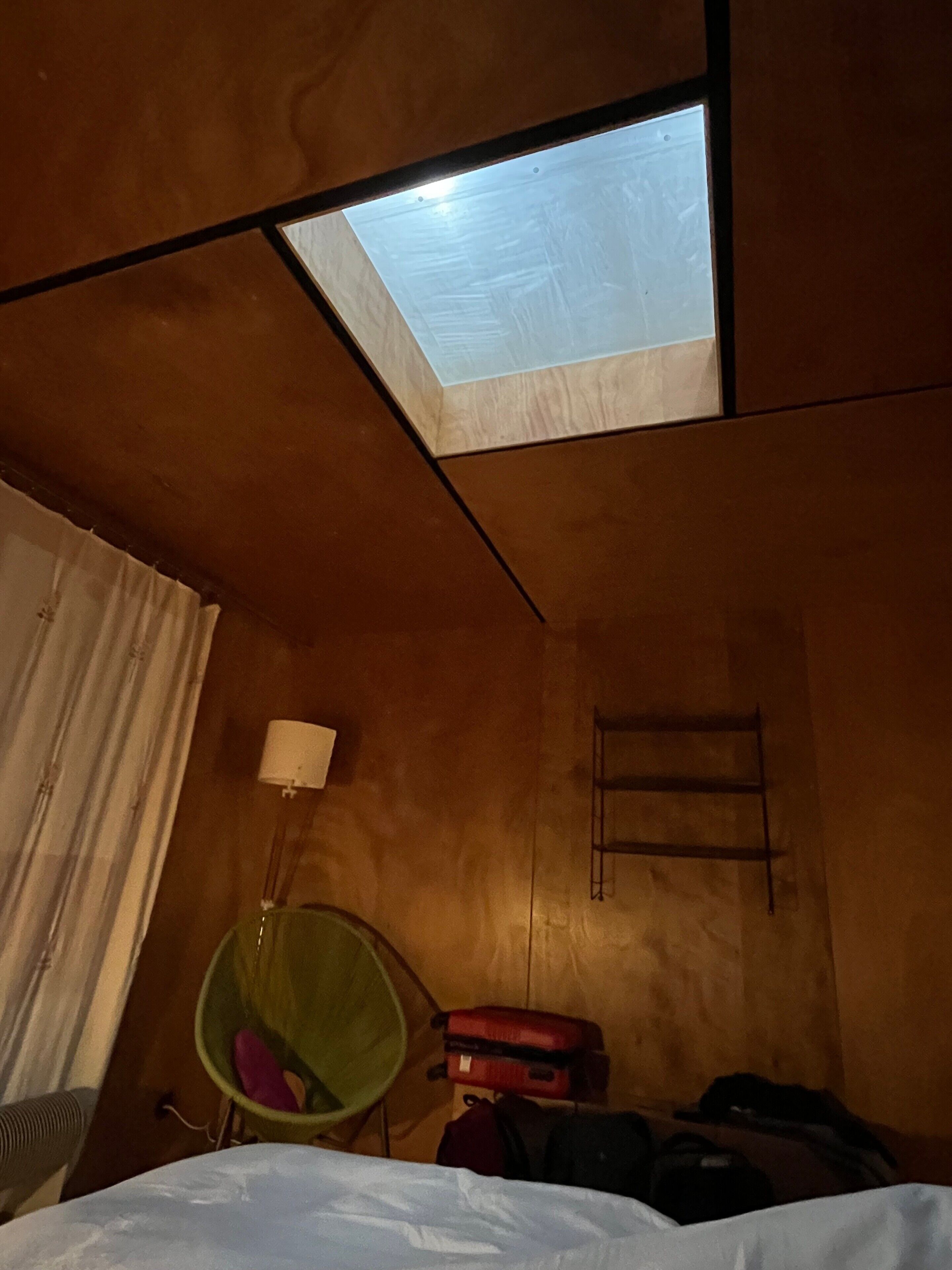 Une pièce avec une lucarne, un fauteuil vert, une valise rouge et une échelle.
