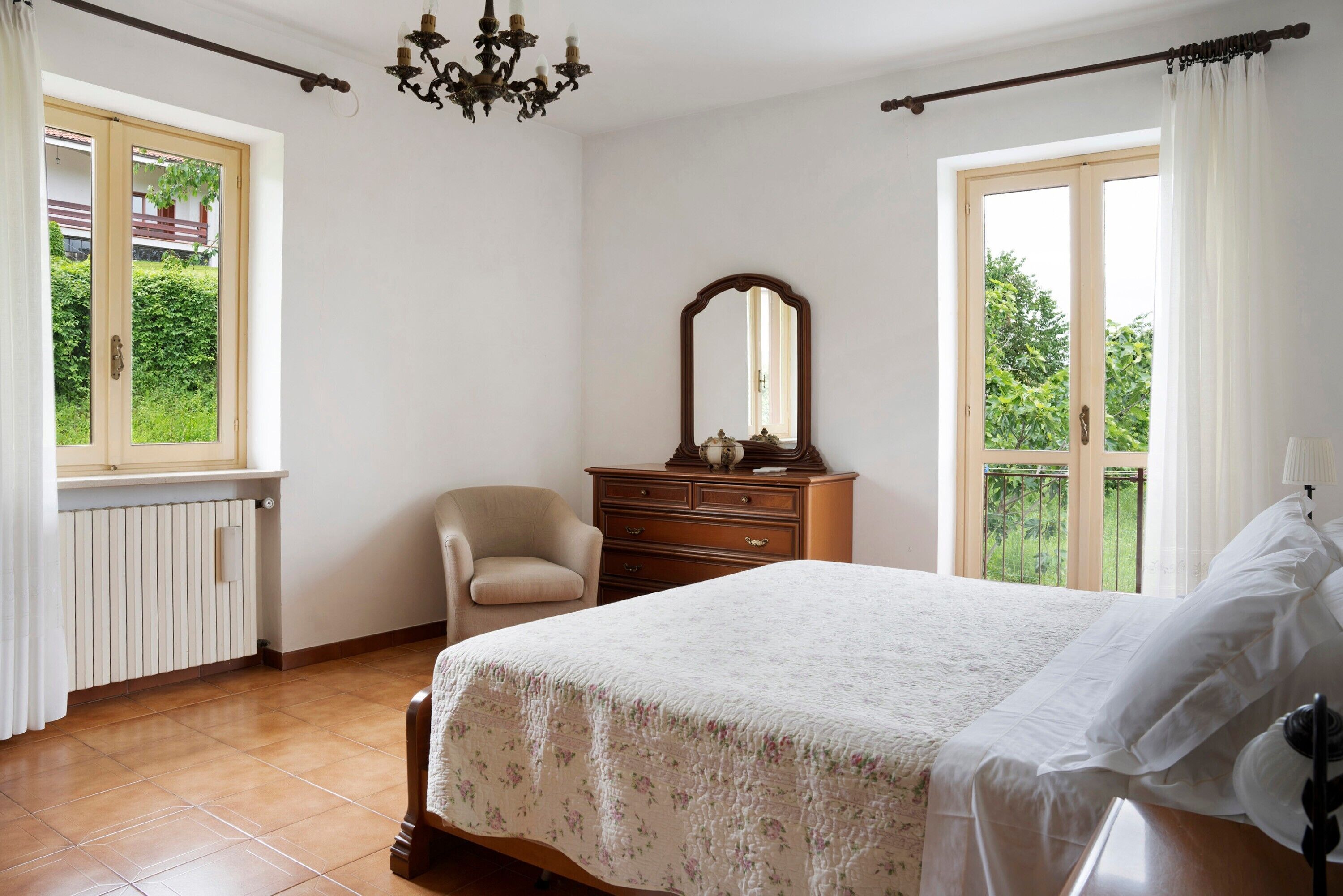 Une chambre à coucher comprenant un lit, une commode, une chaise, un miroir et une fenêtre donnant sur un paysage verdoyant.