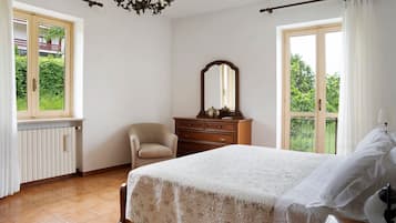 Une chambre à coucher comprenant un lit, une commode, une chaise, un miroir et une fenêtre donnant sur un paysage verdoyant.