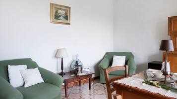 Un salon avec deux fauteuils verts, une table basse en bois, un vase blanc et un tableau encadré accroché au mur.