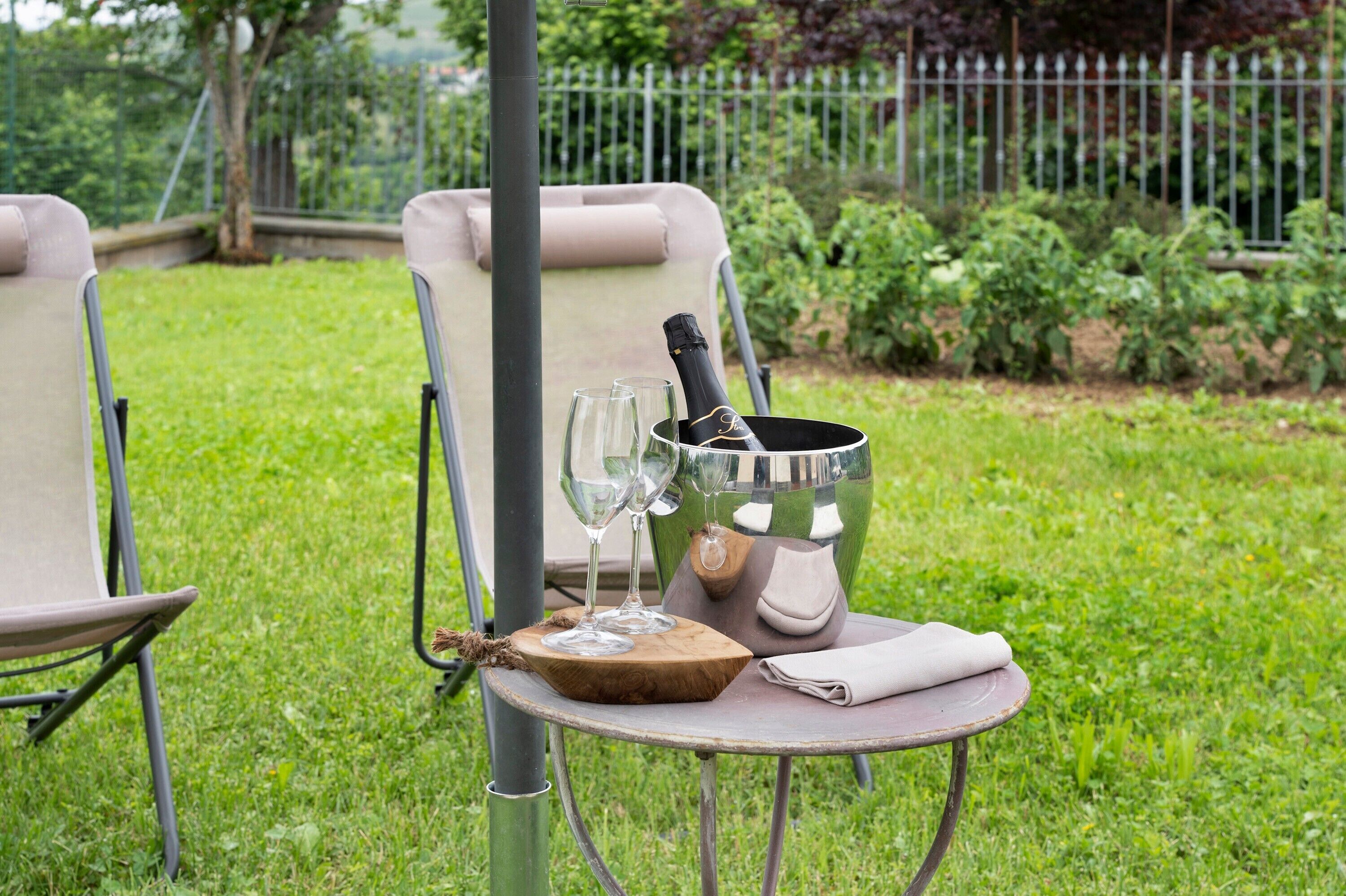 An outdoor seating area with a table, two chairs, a bottle of champagne, and glasses.