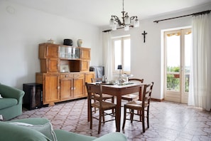 Uma área de refeições com mesa e cadeiras de madeira, um armário com portas de vidro, uma televisão e um candelabro.