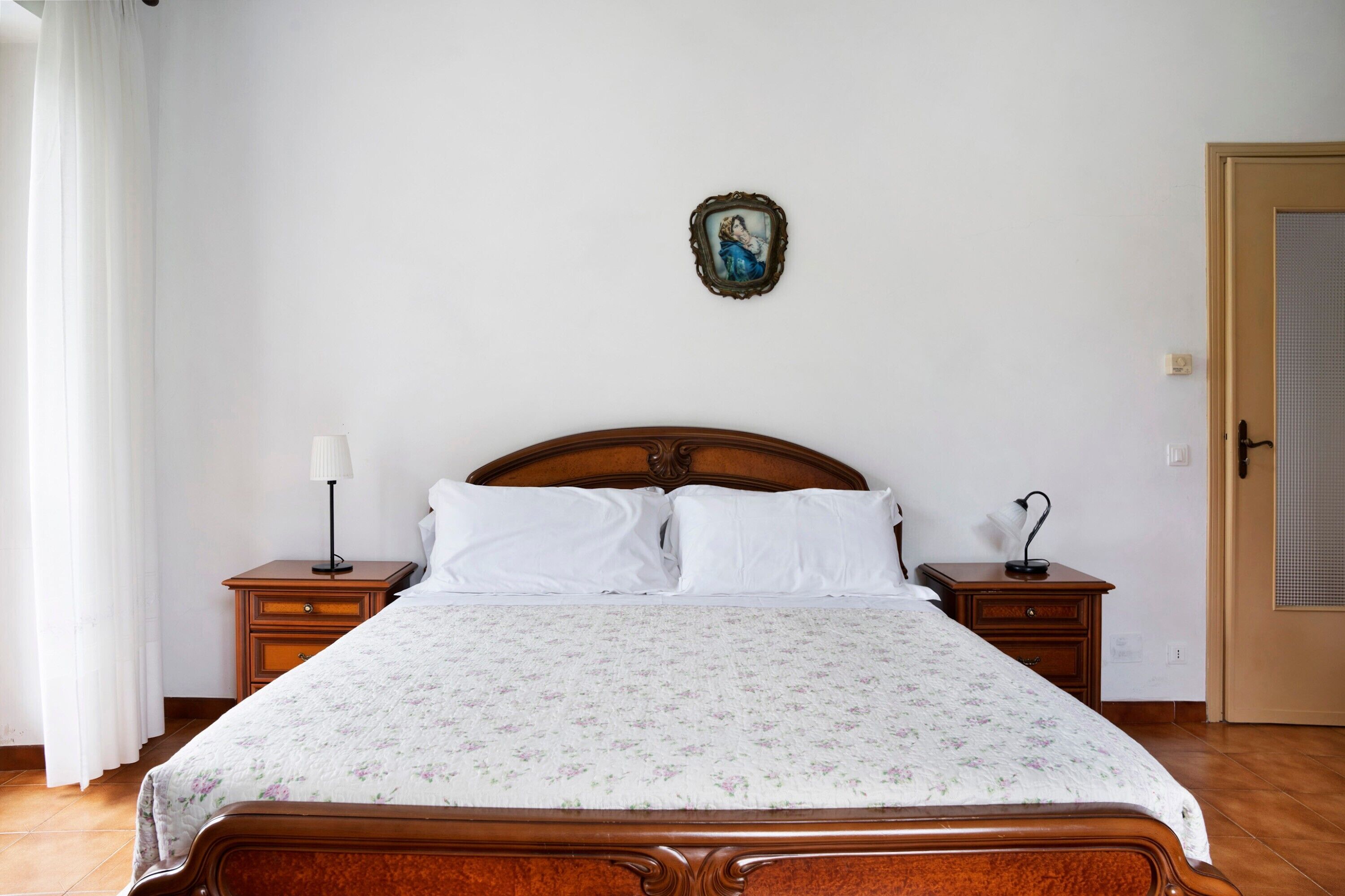 Una camera da letto con un letto in legno, biancheria bianca, un comodino con una lampada, un tavolino con una lampada e una porta.