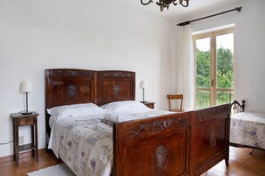 A bedroom with a wooden four-poster bed, two bedside tables, a chair, and a window with a view of greenery. - Holiday Home 'Casa Pianezzo Dogliani' with Mountain View, Private Pool and Wi-Fi (Dogliani)