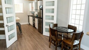 A compact kitchen with white cabinets, a stainless steel refrigerator, and a round table with chairs. - Morel Executive Suites (Edmundston)