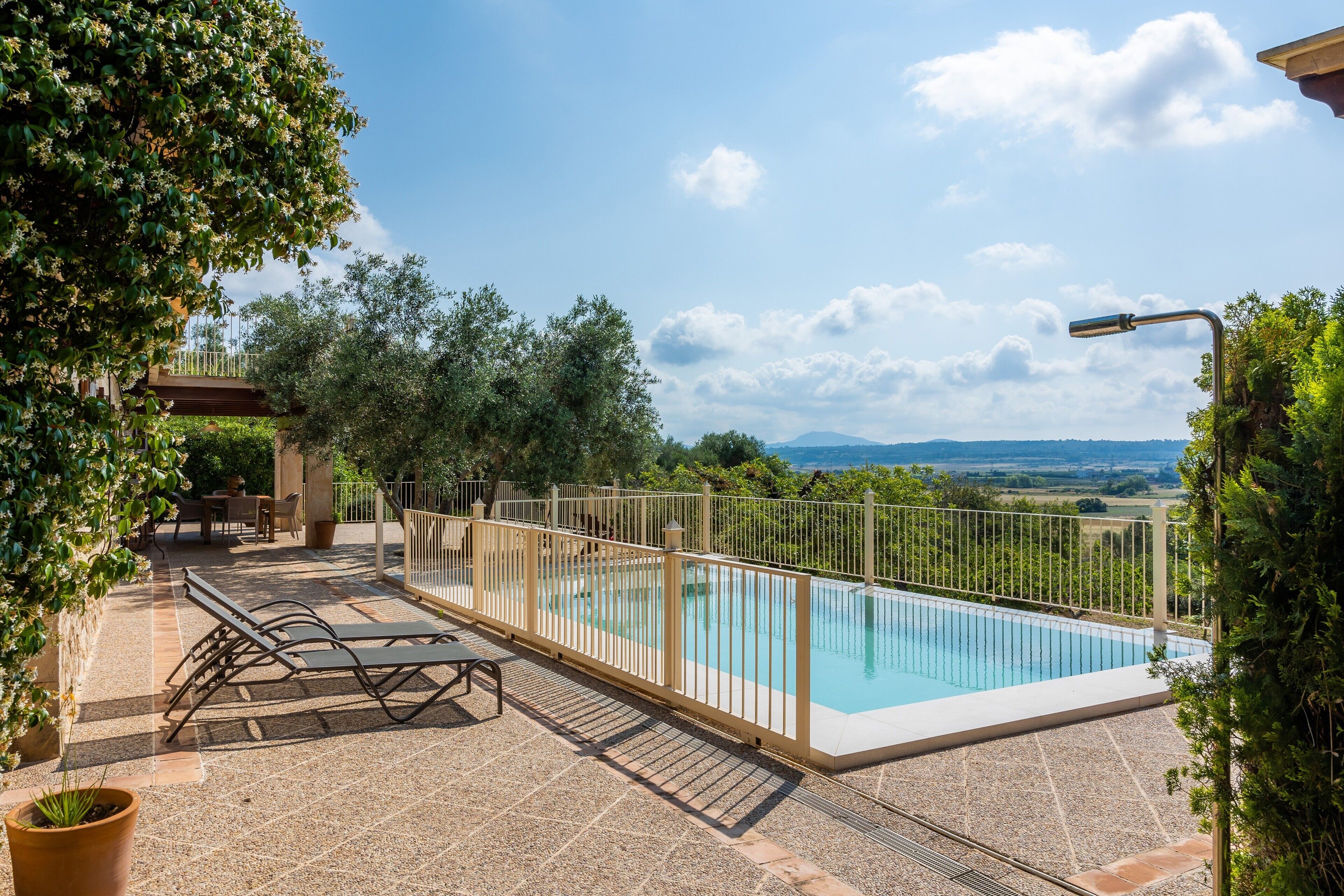 Une piscine entourée d’une clôture, avec un espace extérieur aménagé et une vue sur la campagne.