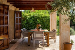 An outdoor patio with a wooden table and chairs, surrounded by greenery and a pergola. - Villa 'Ses Nines' with Mountain View, Wi-Fi and Private Pool (Petra)