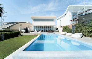 Ett modernt hus med en swimmingpool, utomhusmöbler och en stor entré med glasdörr.
