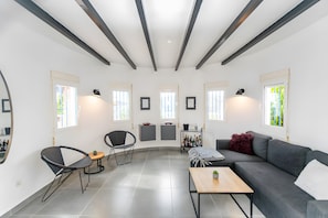 Una sala moderna con un sofá, una mesa de centro, un comedor con sillas y una zona de cocina con un carrito.