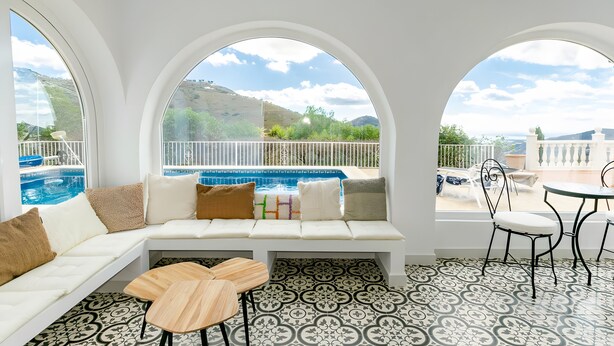 A room with a white sofa, a small wooden table, and a view of a pool and mountains. - Villa "Casa Silencio" with Sea View, Private Pool & Wi-Fi (Cómpeta)