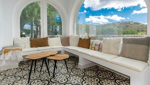 A modern living room with a white sofa, two wooden side tables, and a patterned floor. Large arched windows offer a view of a hilly landscape. - Villa "Casa Silencio" with Sea View, Private Pool & Wi-Fi (Cómpeta)